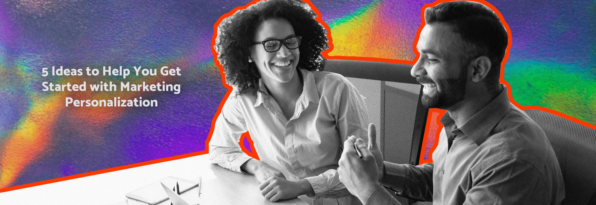 Two co-workers sitting working together at a desk, collaborating and smiling 